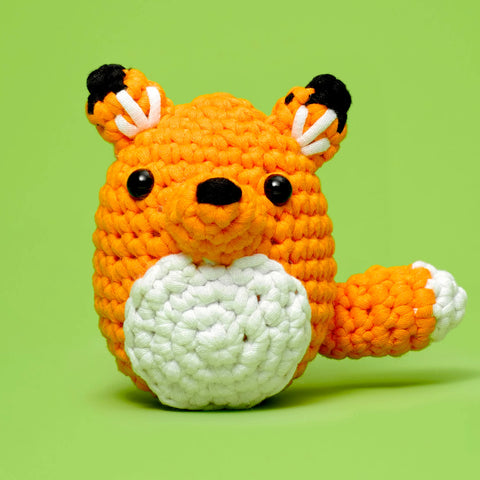 Crocheted fox toy with a white ball on a green background
