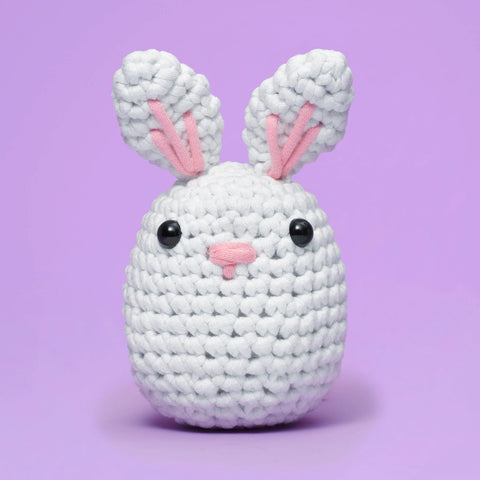 Crocheted bunny toy with pink ears and nose on a purple background